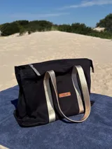 Bolso tipo tote bag negro con detalles dorados en las asas y en el logo.