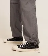 Pantalón cargo negro de corte recto con bolsillos laterales tipo cargo. Presenta cintura elástica con cordón de ajuste y sistema de tiradores en la parte inferior para regular el largo, permitiendo convertirlo en bermuda.