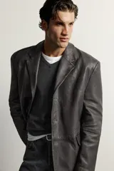 Blazer de cuero marrón oscuro, de corte regular fit, con solapas de muesca, cierre frontal de tres botones y bolsillos con solapa en la cadera.