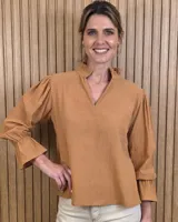Blusa blanca de algodón con escote en V y cuello mao. Presenta mangas largas abullonadas con puños acampanados y fruncidos.