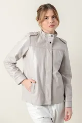 Campera de cuero color gris claro (cemento) con cuello mao abotonado y hombreras. Presenta cierres frontales y bolsillos laterales con ribetes.