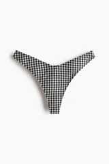 Bombacha de bikini estilo colaless, con tiro bajo y diseño de cintura en V. Presenta estampado de cuadros vichy en blanco y negro.