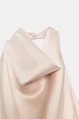 Top de cuello halter con escote fluido y caída suave. Presenta cierre con botones en la parte posterior y diseño sin mangas.