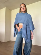 Ruana tejida de algodón con hilo lurex en punto jersey, color azul, con diseño amplio y detalle de etiqueta de cuerina en la parte posterior.