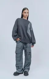 Pantalón cargo técnico gris oscuro, de silueta oversize y tejido liviano. Presenta múltiples bolsillos cargo con solapa en las piernas, uno de los cuales tiene una pequeña etiqueta negra con texto.