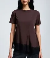 Remera de algodón color marrón chocolate, con cuello redondo, mangas cortas y corte acampanado. Presenta costuras verticales en el frente y un detalle de encaje negro aplicado en el ruedo asimétrico.