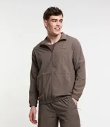 Campera deportiva color marrón, con cuello alto, cierre frontal con cremallera, manga larga, bolsillos laterales y detalles de etiqueta aplicada y rayas.