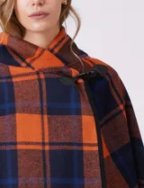 Capa de tejido cuadrille con diseño de cuadros en tonos marrón, beige y naranja. Presenta un cierre frontal con botón tipo trenca y bordes con ribete negro.