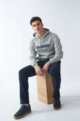 Buzo canguro gris de felpa para hombre con capucha ajustable y cordones blancos. Presenta un logo estampado en el pecho y bolsillo tipo canguro. Corte regular.