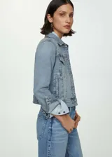 Chaqueta de jean estilo vaquero, con diseño recto y corto. Presenta cuello de solapa, cierre frontal de botones, dos bolsillos laterales y dos bolsillos con solapa y botón en el pecho. Mangas largas con puños abotonados.