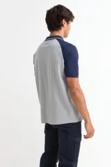 Remera tipo polo de manga corta con diseño combinado, cuerpo en color gris y mangas y cuello en color azul marino. Presenta cierre frontal con botones y detalles de líneas finas en el cuello.