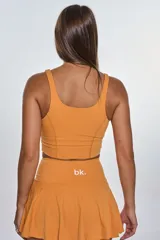 Conjunto deportivo compuesto por un top de escote redondo con logo estampado y una pollera short con tablas. Diseño en color naranja, confeccionado en tejido elástico de secado rápido.
