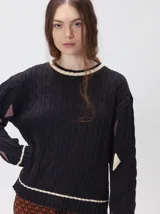 Sweater de punto con diseño de ochos en color verde, cuello redondo con detalle de franja en contraste, y apliques de rombos en las mangas. Presenta un bordado con la letra M en el pecho.