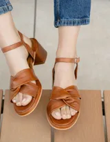 Sandalia de cuero vacuno color marrón, con tiras cruzadas en el empeine, pulsera con hebilla al tobillo, suela de goma y taco cuadrado.