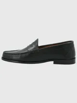 Zapato tipo mocasín de cuero negro con diseño clásico, costuras visibles en la puntera y detalle de antifaz en el empeine.