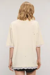 Remera oversize de jersey de algodón en color blanco, con cuello redondo, mangas cortas y largo a la cadera. Presenta estampa frontal con la inscripción "Gypsy Lover", detalles de roturas y apliques de puntilla en las mangas y el ruedo.