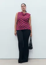 Blusa sin mangas con cuello drapeado, confeccionada en tejido fluido con estampado geométrico en tonos rojos y violetas.