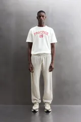 Camiseta de algodón gris melange con cuello redondo, mangas cortas y efecto lavado. Presenta un estampado de texto frontal en color oscuro con efecto desgastado.