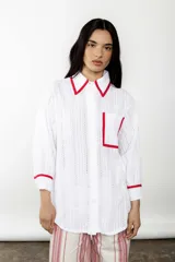 Camisa blanca de broderie con detalles en bies rojo, corte amplio y estilo relajado.