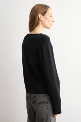 Chaqueta de tejido de punto color negro, con cuello redondo y cierre frontal mediante alamares metálicos. Presenta mangas largas con puños rectos y un corte recto.