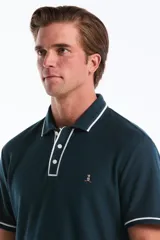 Polo de manga corta en tejido mesh color verde oscuro, con cuello y tapeta de botones en contraste con ribete blanco. Presenta el logo del pingüino bordado en el pecho.