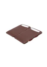 Billetera artesanal de cuero marrón oscuro con costuras en hilo rojo. Presenta un sistema de sujeción elástico en el lateral con detalles de colores (rojo, amarillo, azul) y ranuras para tarjetas en el exterior.