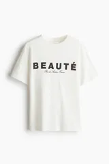 Remera de algodón color blanco crudo, con cuello redondo y manga corta. Presenta un estampado frontal con la palabra "BEAUTÉ" en mayúsculas y debajo en cursiva "Rue des Artistes France".