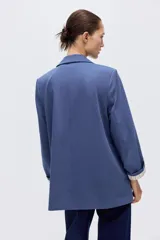 Blazer de sarga color azul, sin cierre, con solapas de pico, bolsillos delanteros con solapa y mangas largas.