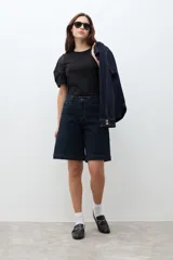 Bermuda de jean en color azul oscuro, de corte recto y largo hasta la rodilla, con diseño clásico de cinco bolsillos y cierre frontal con botón y cremallera.
