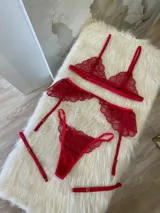 Conjunto de lencería de tres piezas en encaje rojo, compuesto por un bralette triangular, una tanga regulable y un portaligas con volados en las caderas.
