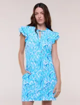 Vestido corto de playa con protección solar UPF 50, color celeste con estampado abstracto blanco y azul. Cuenta con escote en V con cordón ajustable, mangas cortas con volados dobles y prácticos bolsillos laterales.
