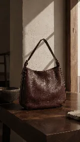 Cartera tipo hobo de cuero premium con textura natural, diseño amplio y minimalista. Cuenta con una correa regulable para llevar al hombro y cierre superior.