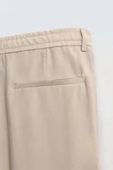 Pantalón de corte relajado confeccionado en tejido con mezcla de lyocell. Presenta cintura con trabillas, cierre frontal con cremallera y botón, pliegues en el delantero, bolsillos laterales y bolsillos traseros de vivo.