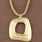 Collar con cordón trenzado color beige y dije grande de metal dorado con forma orgánica irregular y agujero central.