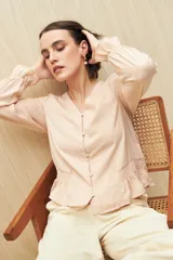 Camisa negra de manga larga con escote en V y botones forrados al tono en el frente. Destaca por su textura sutil y por el detalle de frunces con volados en la parte inferior.