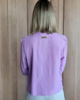 Camisa de manga tres cuartos color beige con cuello con volados y botones frontales. Presenta un detalle de color negro en la parte superior de las mangas.