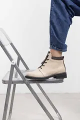 Borcego de cuero vacuno color marrón caramelo con acabado mate, estilo combate y caña baja. Cuenta con cordones marrones, panel de gamuza oscura en el cuello y suela de caucho negra tipo tractor con costura blanca visible.