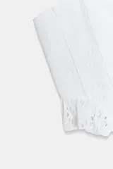 Top corto blanco de escote recto y tirantes finos. Presenta detalles de bordados perforados combinados a tono y un ruedo con volado.