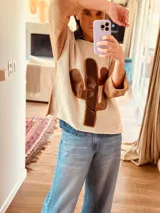 Sweater de punto color crema con mangas color camel y aplique de cuero marrón en forma de cactus en el frente.