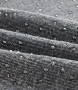 Pantalón de jean de corte recto y tiro medio, color gris con acabado lavado y aplicaciones de brillos distribuidas en las piernas. Cuenta con diseño de cinco bolsillos, cierre frontal con botón y costuras reforzadas.