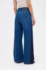 Jean de corte wide leg con diseño bicolor, combinando un tono de denim azul medio en el frente y un tono azul oscuro en los laterales. Presenta cintura alta, cierre frontal con botón y bolsillos laterales.