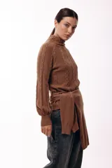 Polera de tejido de punto color marrón, con cuello alto y diseño de trenzas verticales. Presenta mangas largas con puños ajustados y un detalle de panel lateral asimétrico que se anuda en la cintura.