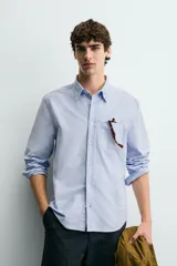 Camisa de corte regular fit confeccionada en tejido de algodón tipo Oxford. Presenta cuello abotonado, manga larga con puños abotonados, bolsillo frontal en el pecho y cierre de botonadura central.
