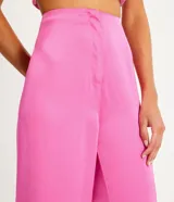 Pantalón pantalona negro con textura satinada, corte de barras amplias, cierre de botón y cremallera, y pinzas.