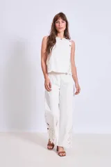 Blusa blanca sin mangas, de corte recto y escote redondo, con detalles de bordados calados en los bordes y los hombros.