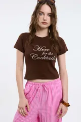 Remera blanca de algodón con corte al cuerpo, mangas cortas y cuello a la base. Presenta una estampa localizada en el frente con el texto "SUMMER GARDEN" en azul y un diseño floral en tonos rosados.