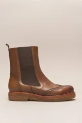 Bota tipo Chelsea de cuero vacuno color suela, con diseño brogue en la puntera y laterales. Presenta paneles elásticos laterales en color marrón oscuro, tirador trasero y suela de goma con plataforma.