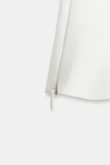 Top de cuello halter con escote corazón, confeccionado en tejido satinado. Presenta cierre lateral con cremallera oculta y botones en la espalda.