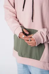Buzo tipo canguro con capucha, confeccionado en una combinación de algodón rústico y microfibra. Presenta un diseño bicolor en tonos rosado y verde militar, con bolsillo frontal tipo canguro en contraste, cordones ajustables y estampa personalizada en el frente.