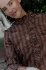 Camisa de corte clásico con estampado de rayas verticales, cuello alto con volados frontales y mangas largas con puños con volados.